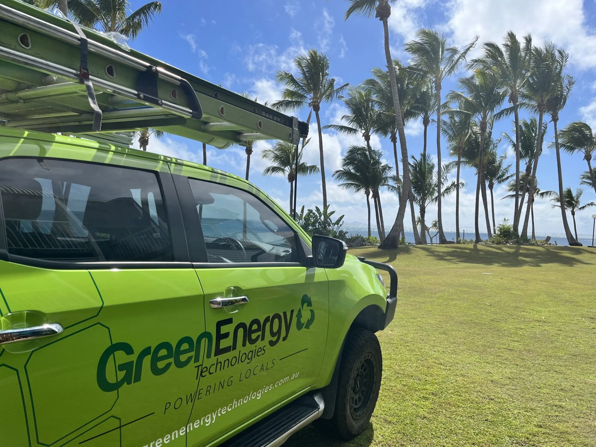 Green Energy Technologies service vehicle parked near a tropical coastline, delivering sustainable solar panel solutions to local communities