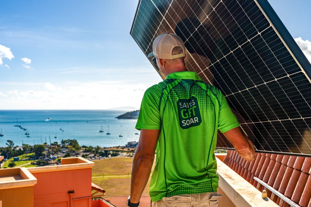 GET installer carrying a solar panel above the Whitsundays coastline